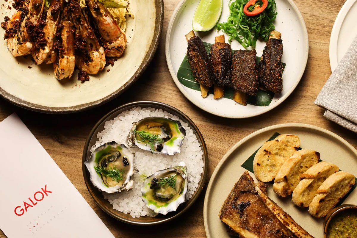 An overhead view of oysters, grilled prawns, ribs, bread and a roasted bone beside a restaurant menu.