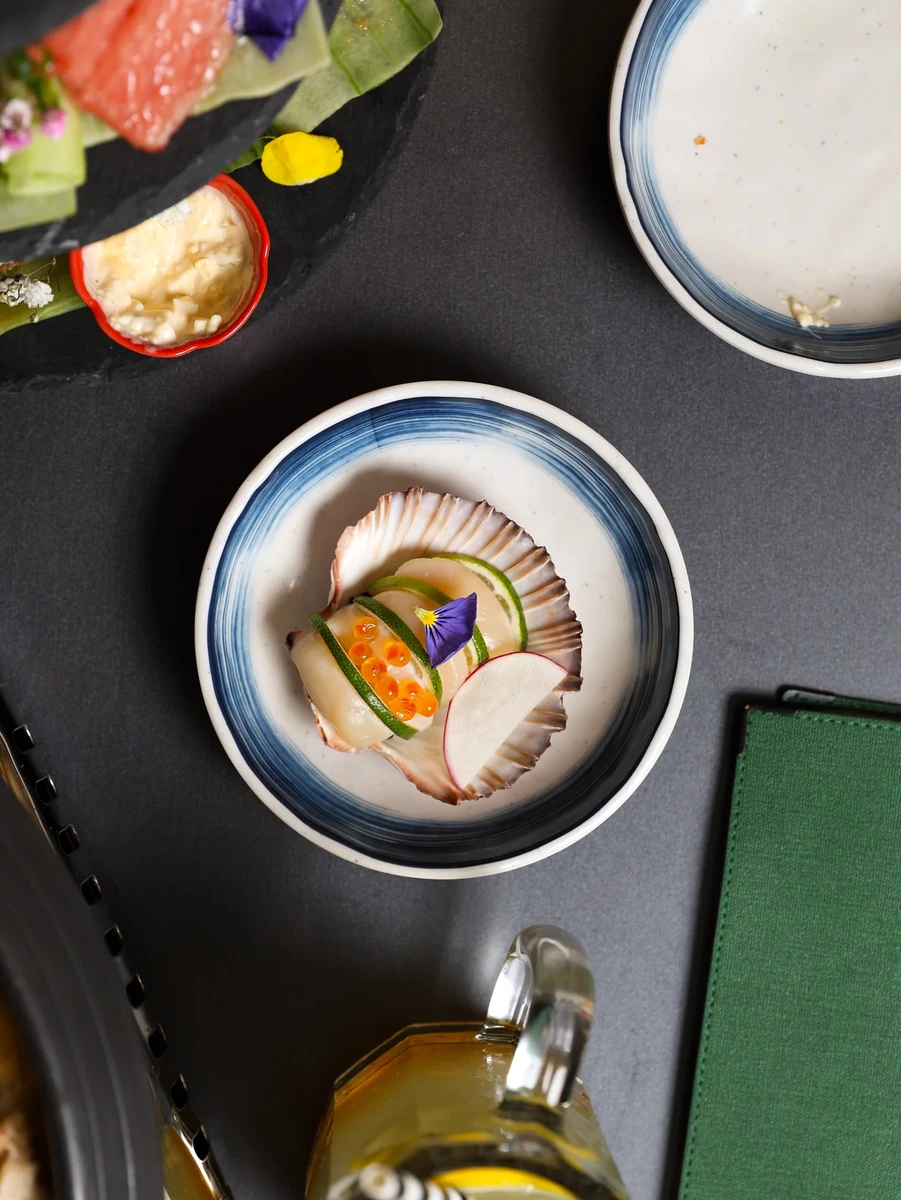 A small blue-rimmed plate holds neatly arranged pale slices and a flower garnish on a dark tabletop.