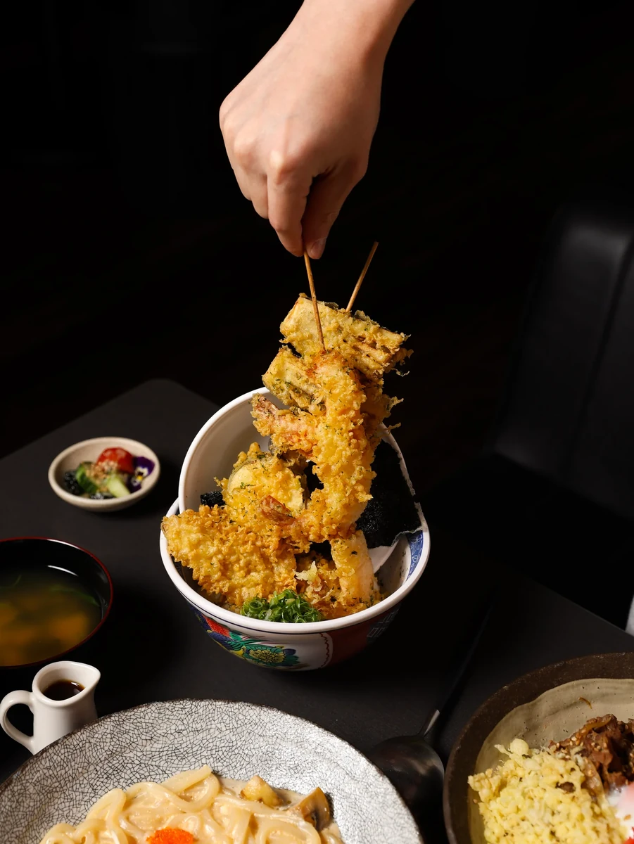 A hand lifts a tall stack of golden battered pieces above a patterned bowl.