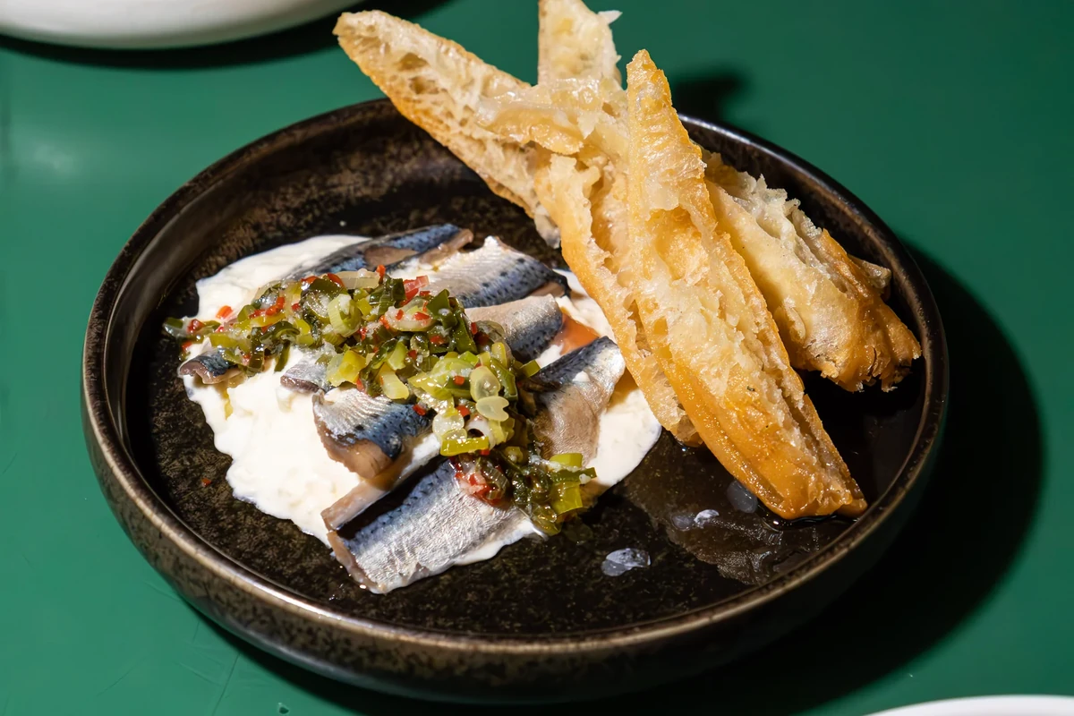 A dark plate with small fish and crisp fried pieces on a green tabletop.