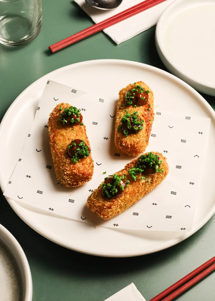 Two golden topped bites on a white plate with red chopsticks nearby.