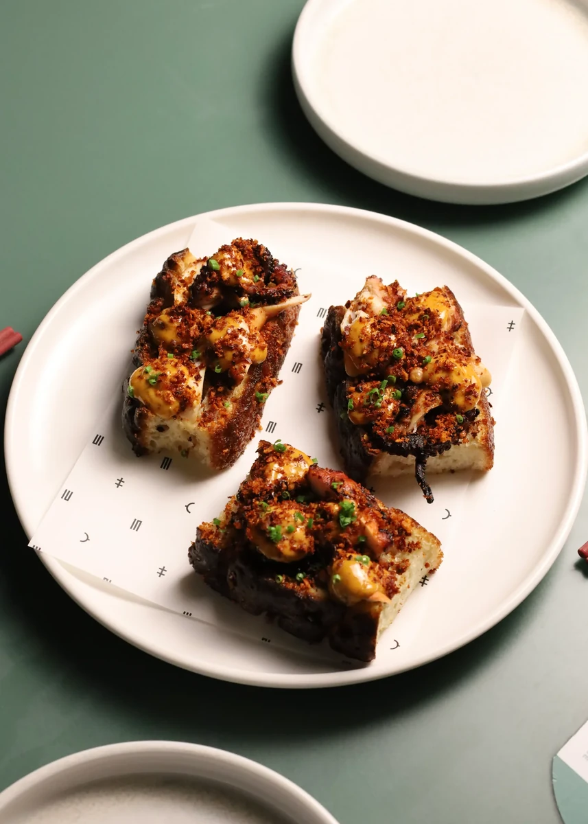 Three toasted pieces topped with a dark savoury mixture on a white plate.
