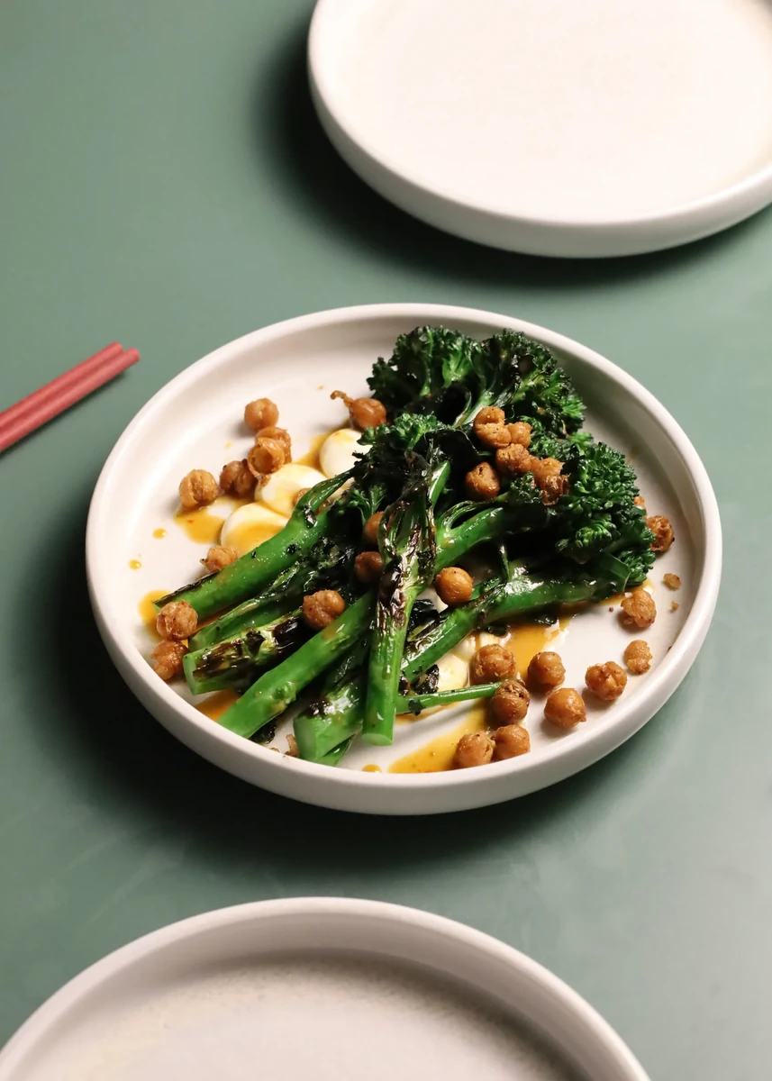 Green vegetables with sauce and crispy toppings on a white plate.