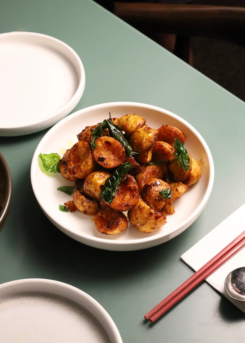 A white bowl of glazed round bites beside red chopsticks.