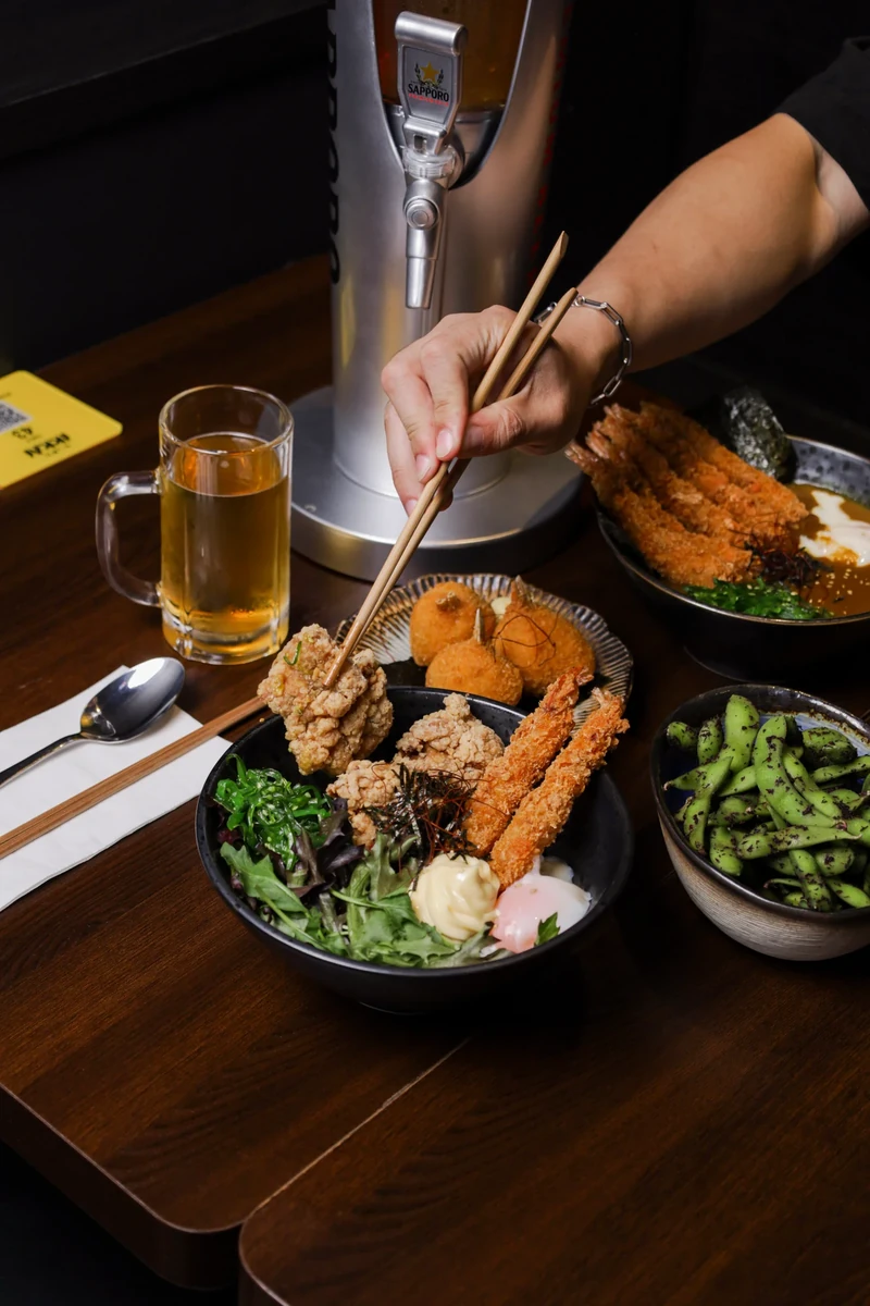 A hand uses chopsticks to pick food from a platter of fried pieces and salad.