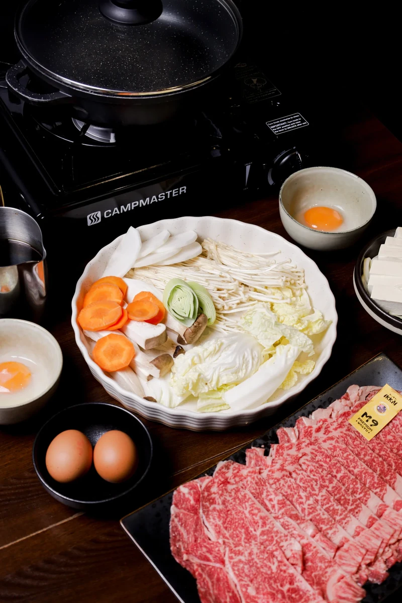 Sliced beef, vegetables and eggs arranged beside a portable tabletop cooker.